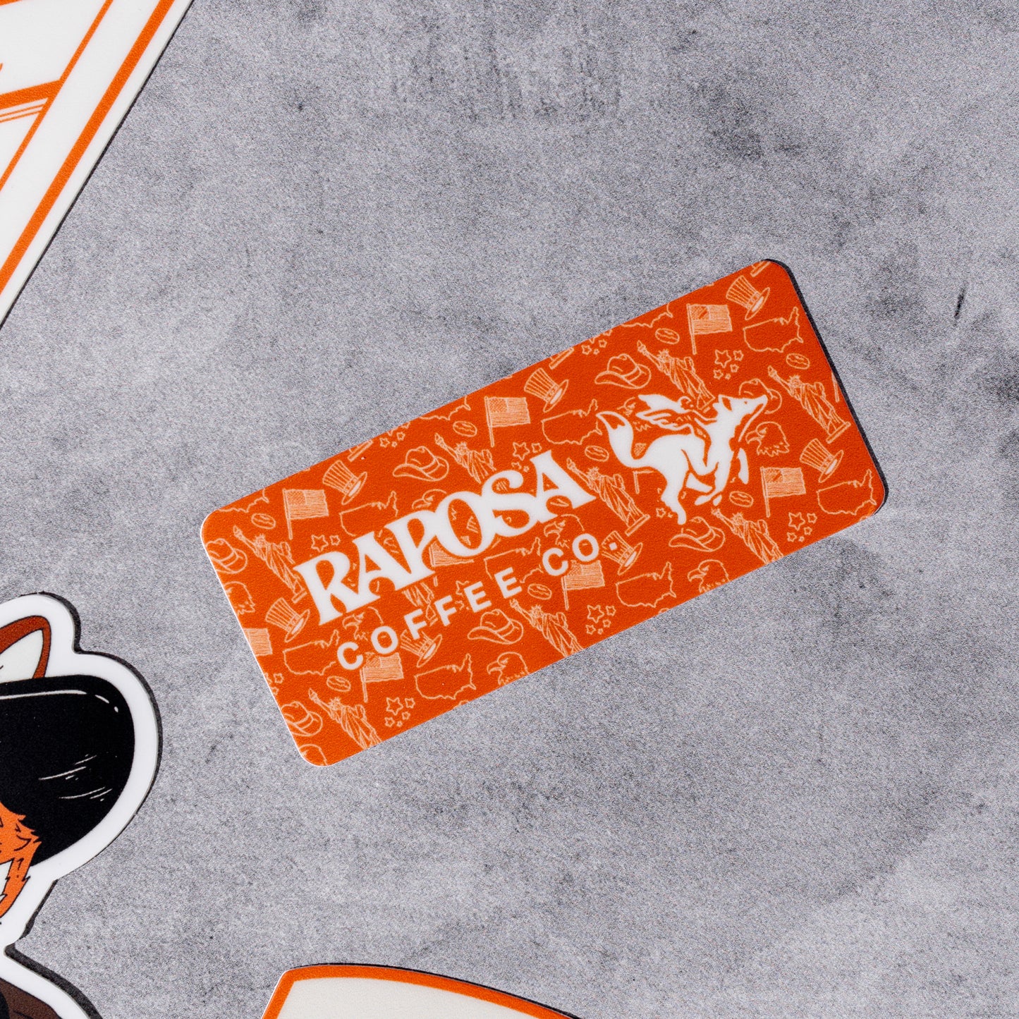 Orange 'Raposa Coffee Co' vinyl sticker with brand logo on a gray surface