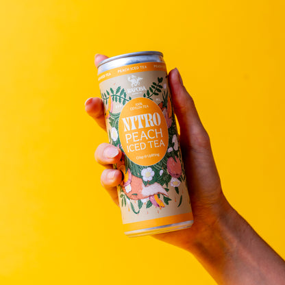 Hand holding a can of Raposa 'Nitro Peach Iced Tea' against a yellow background